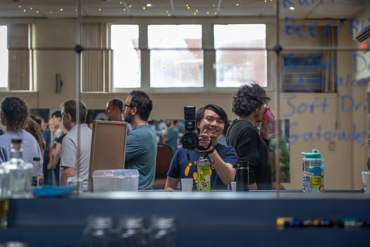 Kang Kang photographing behind the counter at a swing dance social, camera raised